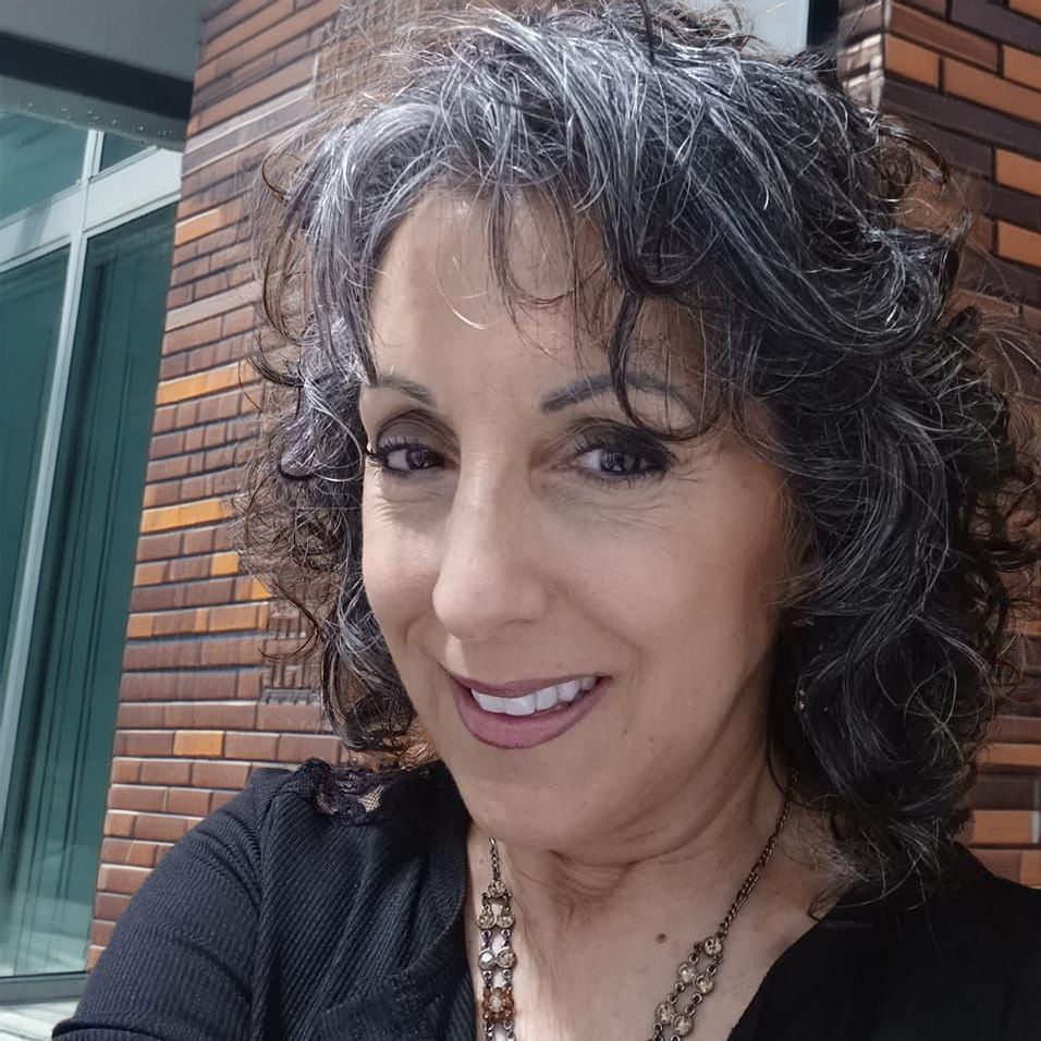 A woman with gray hair is smiling and wearing a black shirt and necklace.