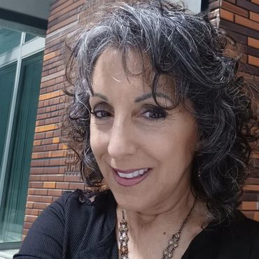A woman with gray hair is smiling and wearing a black shirt and necklace.