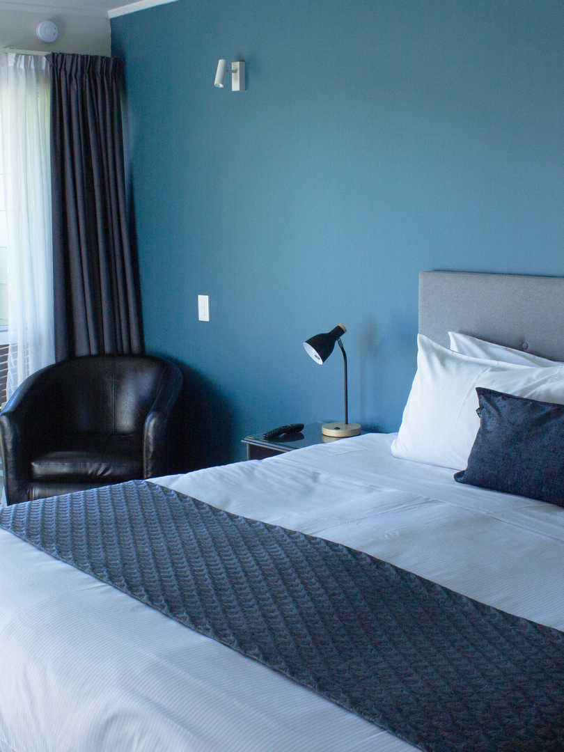 A hotel room with a bed , chair , lamp and blue walls.