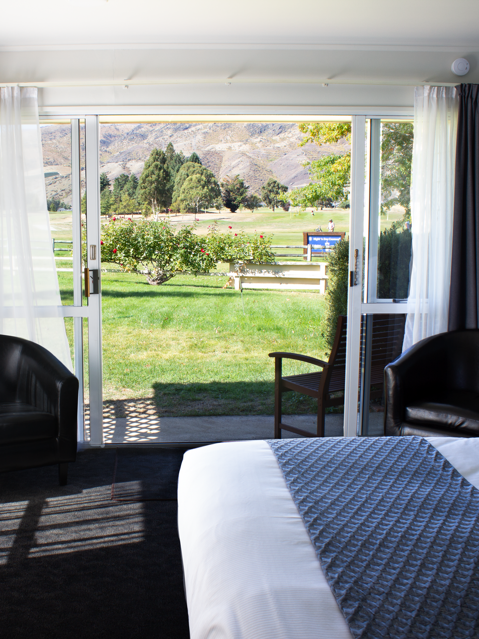 A hotel room with a bed , chairs and sliding glass doors leading to a lawn.