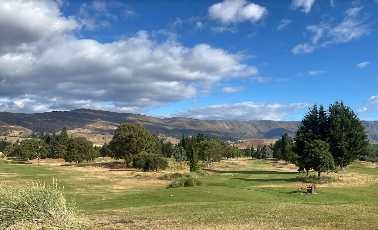 Golfers enjoying a round at Cromwell Golf Course, surrounded by lush green fairways and scenic mountain views on a sunny day