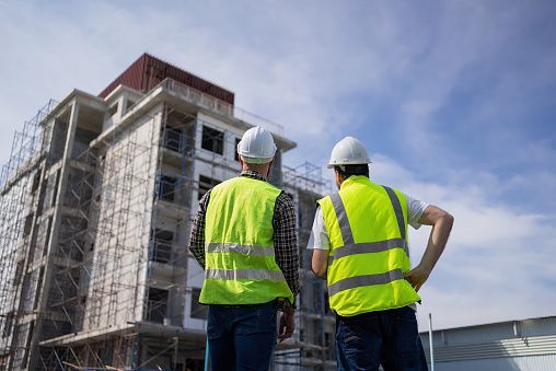 Two construction workers are standing in front of a building under construction.