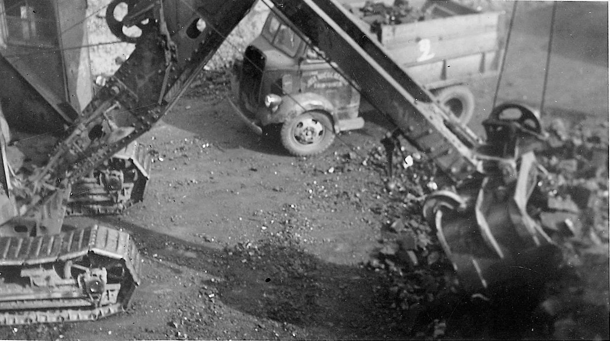 A black and white photo of a excavator digging a hole in the ground.