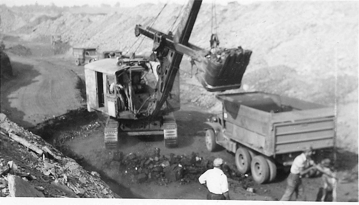 A black and white photo of a dump truck being loaded with dirt.
