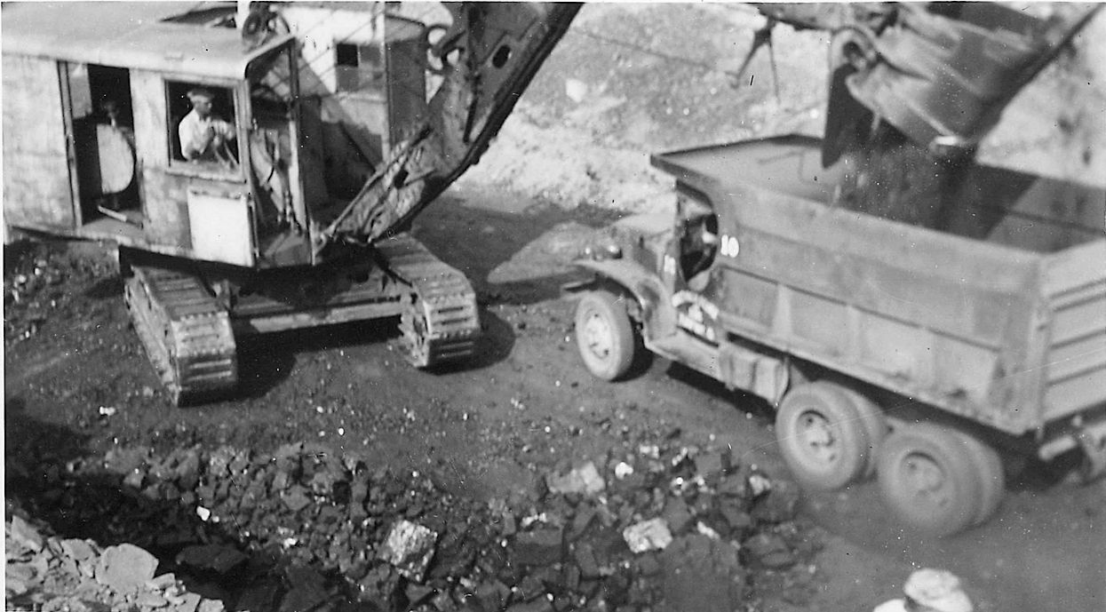 A black and white photo of a dump truck being loaded with dirt.
