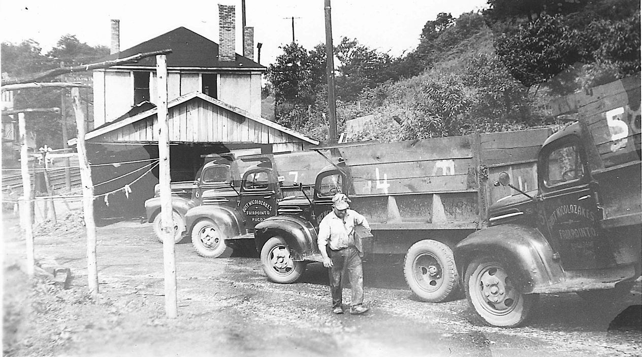 A black and white photo of a man standing next to a dump truck.
