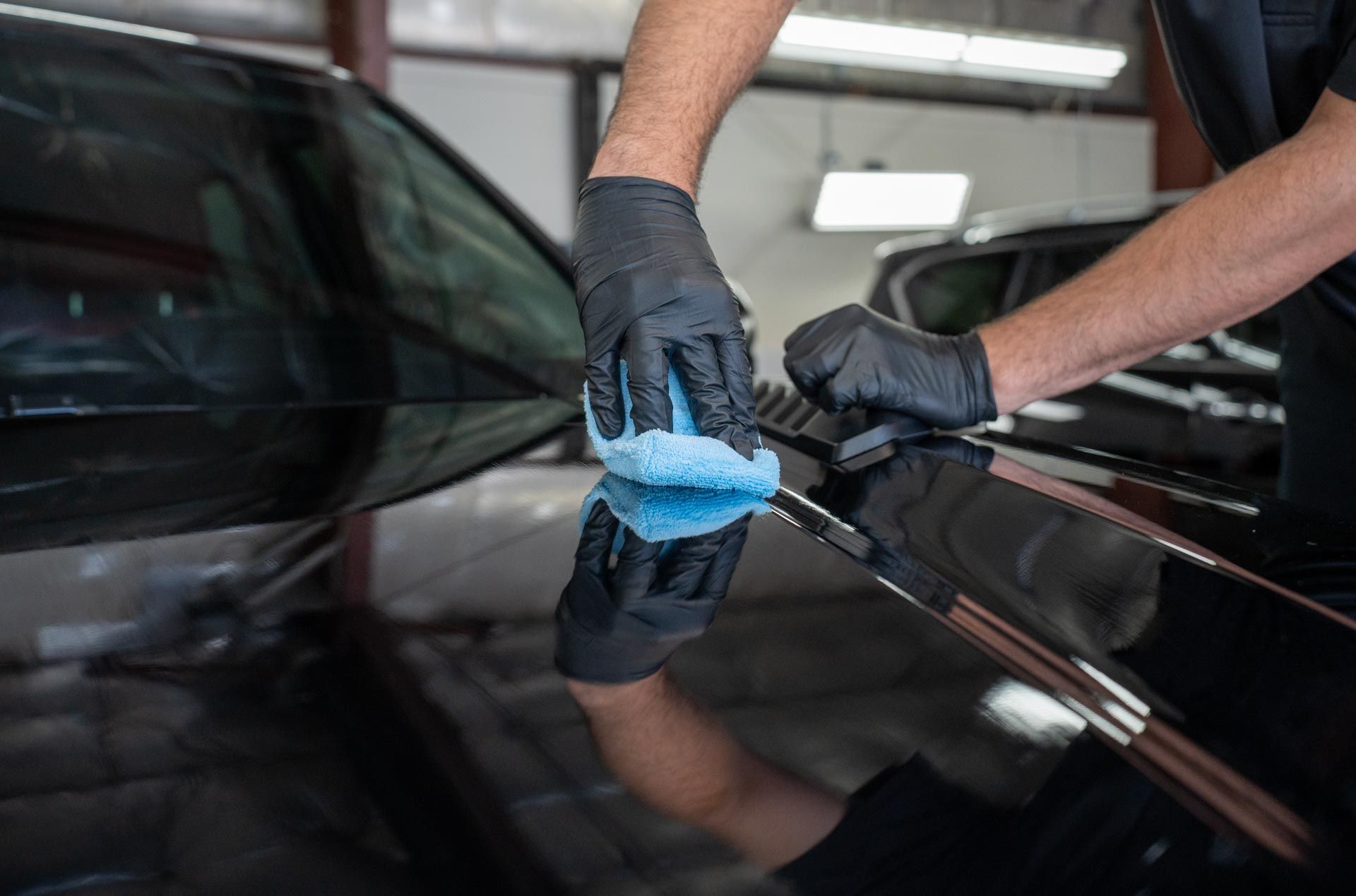 A man is applying ceramic coating to the hood of a car with a sponge.
