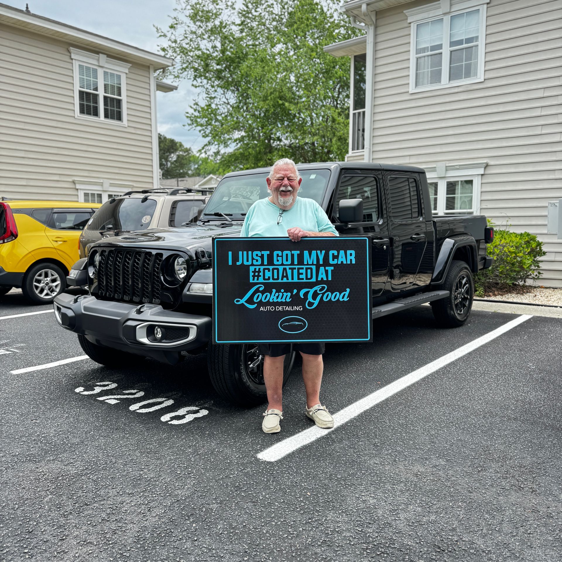 Man holding sign in front of black Jeep truck, parked in front of condos.