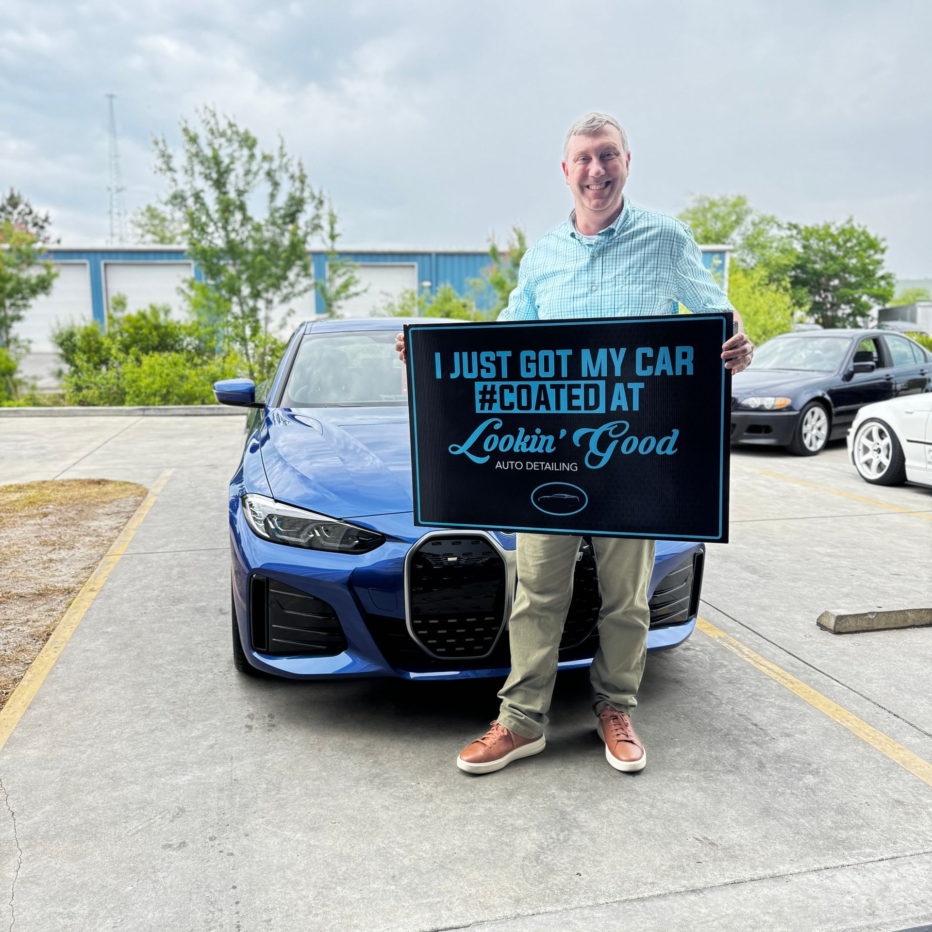 Man holding sign next to blue car. Sign says 