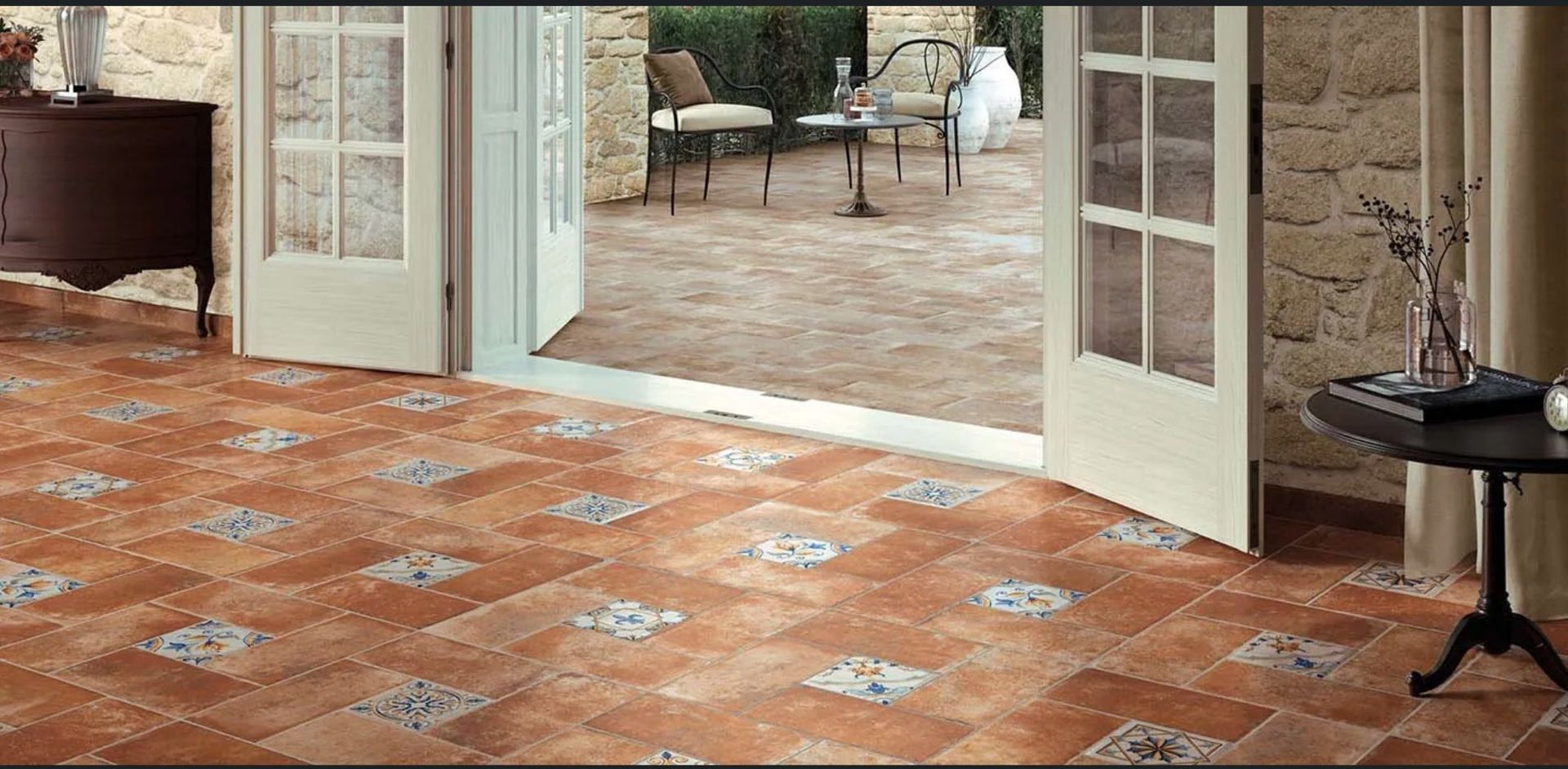 Interno con pavimento in cotto, porte aperte che conducono a un patio con mobili da esterno.