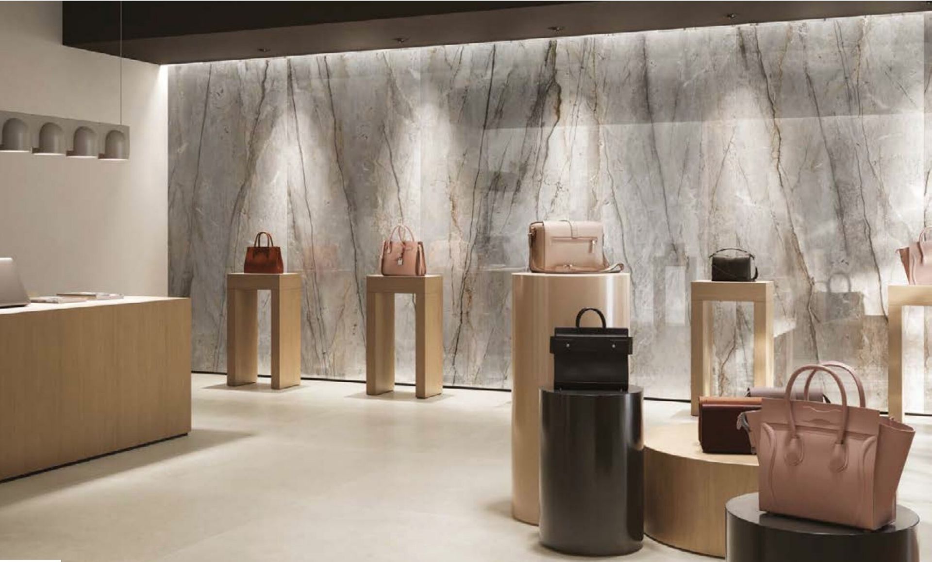 Interno di una boutique con borse di lusso esposte su piedistalli contro una grande parete di marmo.