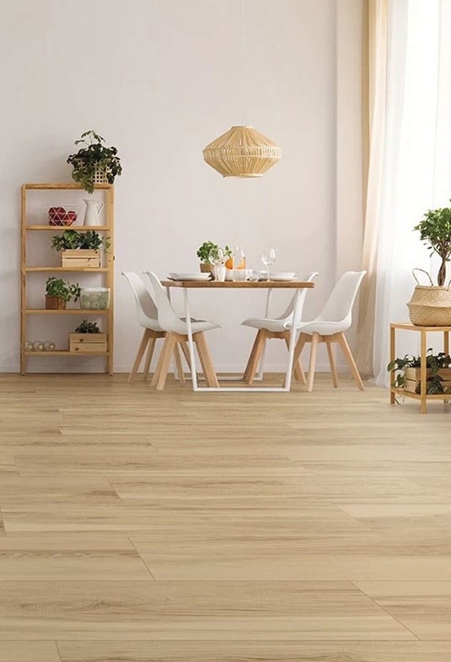 Sala da pranzo con pavimento in legno chiaro, tavolo, sedie bianche, piante e lampada a sospensione intrecciata.