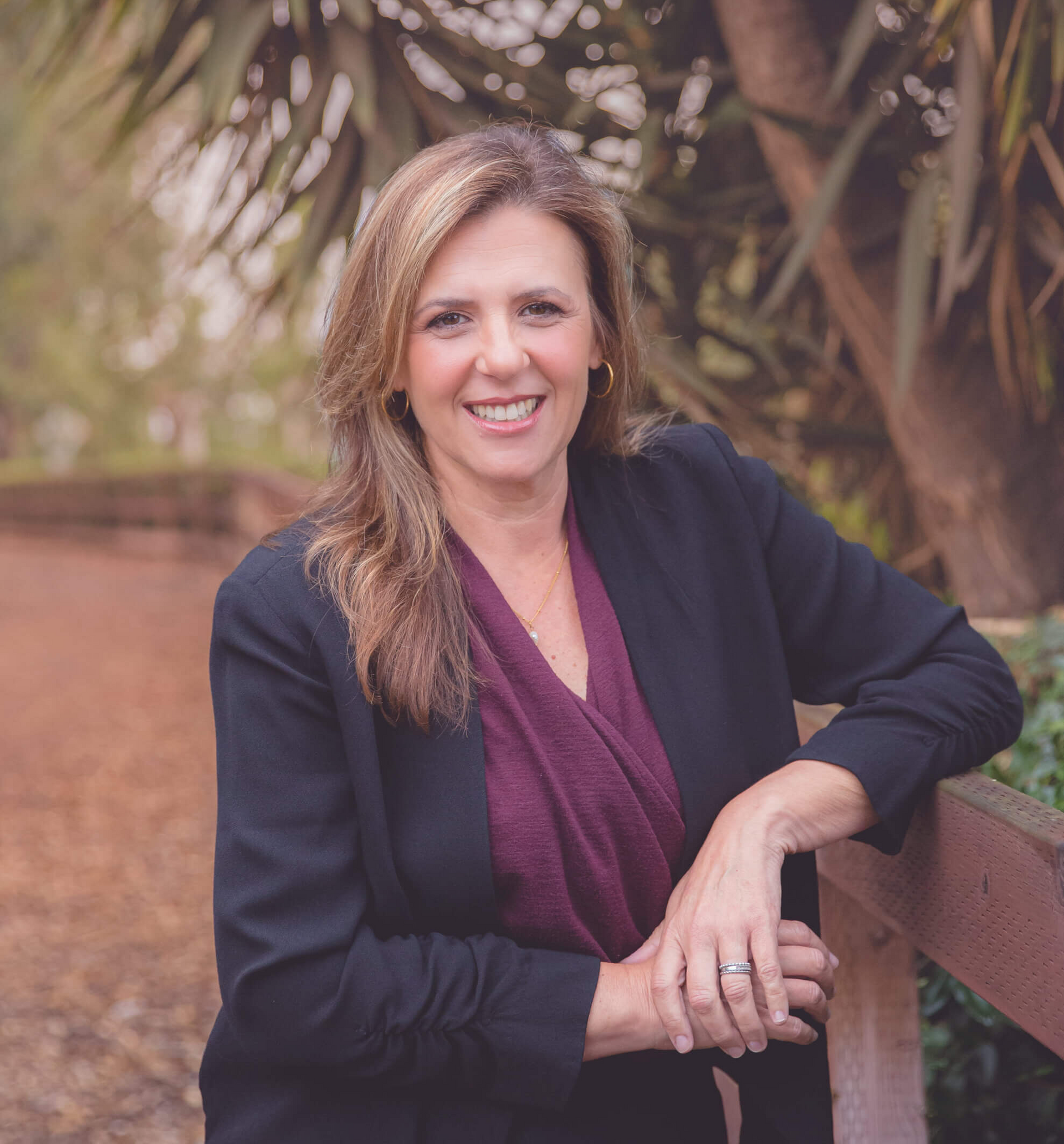 A woman in a black jacket and purple top is leaning on a wooden fence.