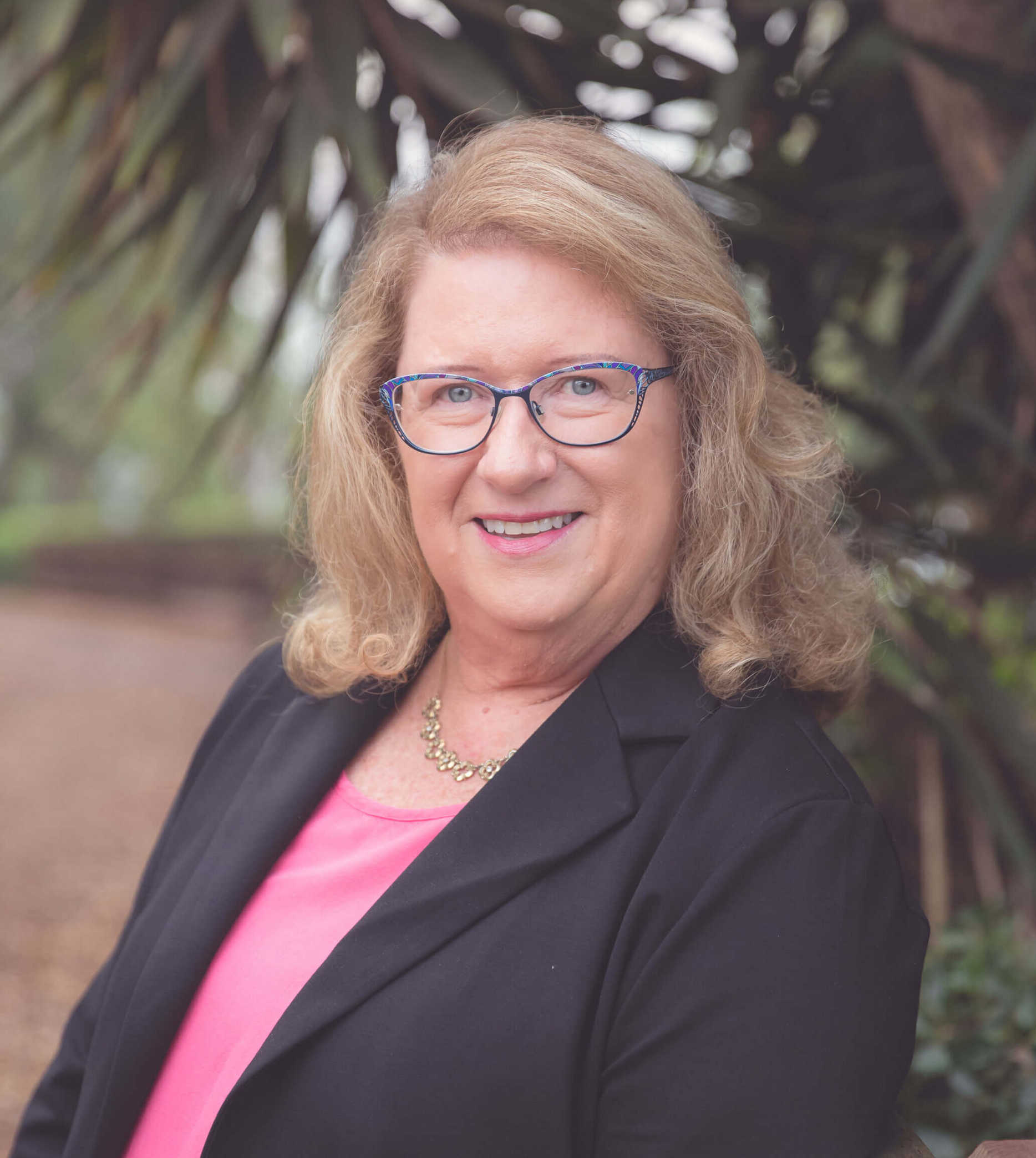 A woman wearing glasses and a black jacket is smiling for the camera.