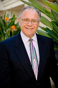 A man in a suit and tie is standing in front of a plant.
