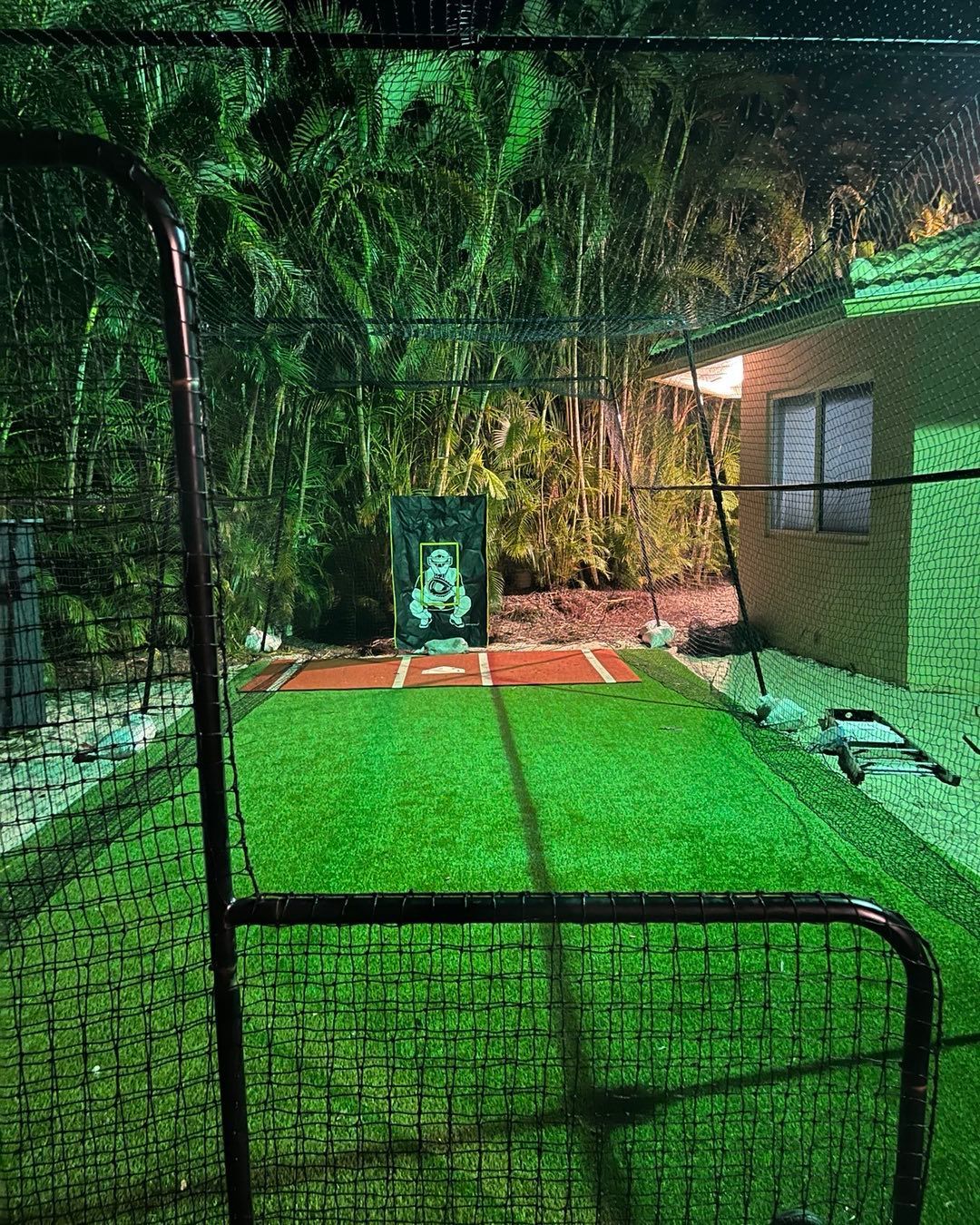 A baseball field with a fence and a house in the background at night.