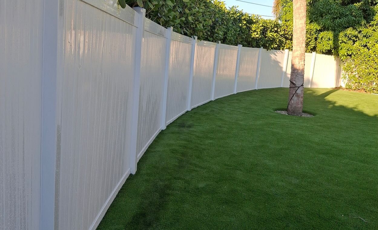 A white fence surrounds a lush green lawn in a backyard.
