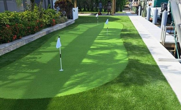 A putting green is sitting on top of a lush green lawn next to a dock.