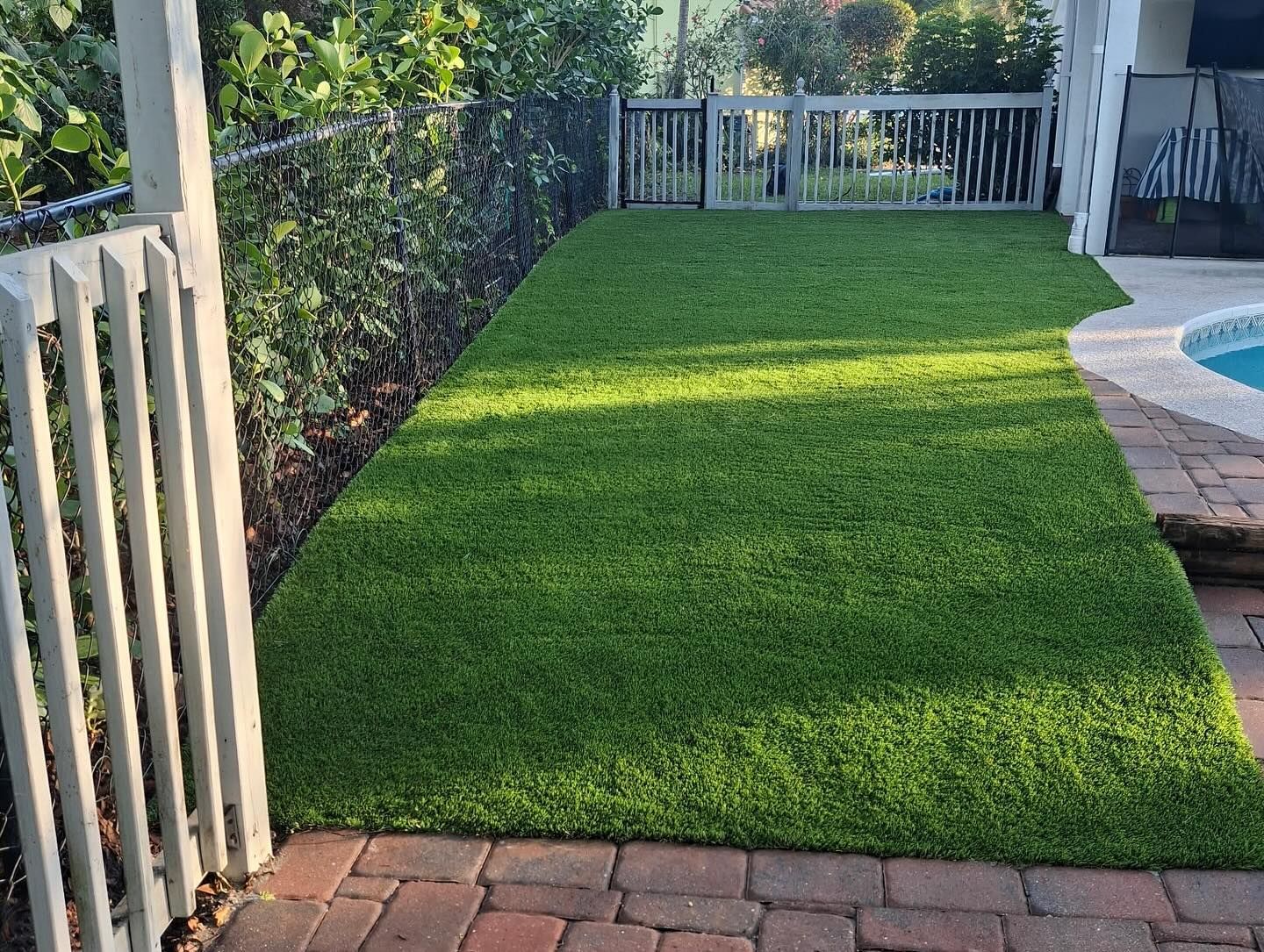 A lawn with a fence and a pool in the background.