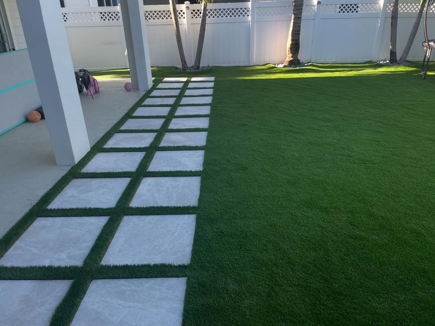 A lawn with a walkway going through it and a white fence.