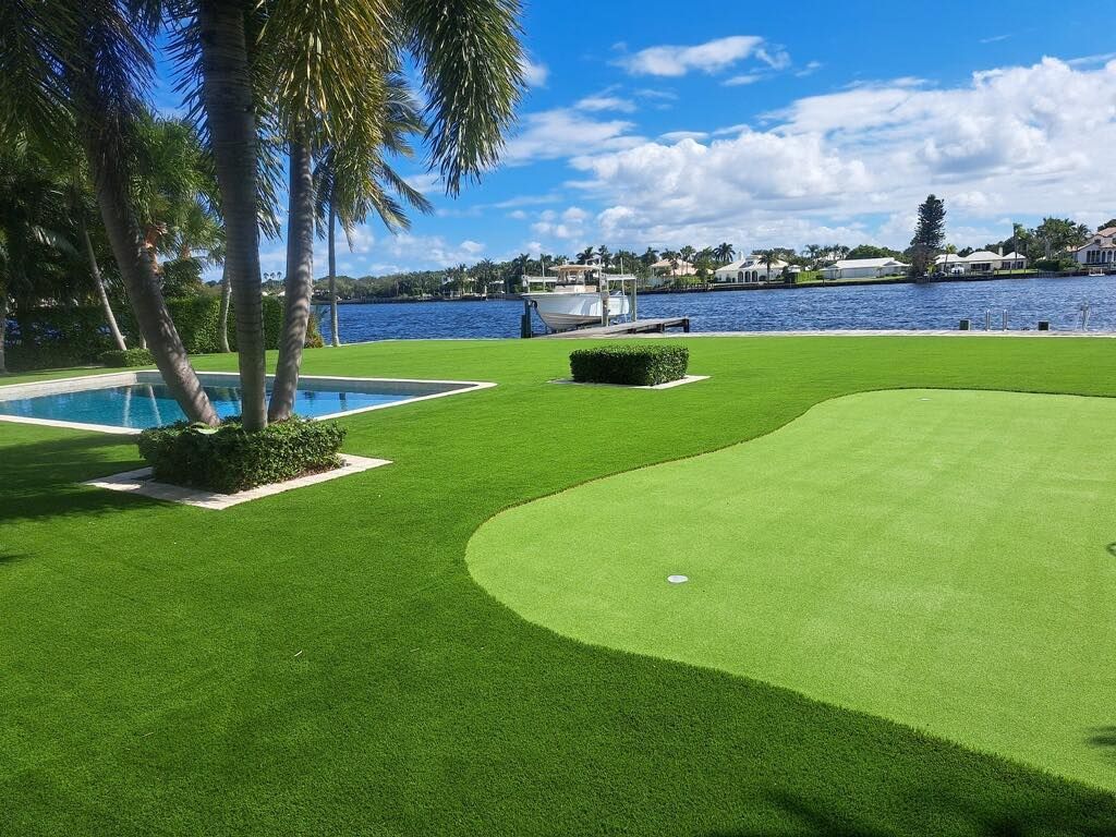 A lush green lawn with a putting green and a pool in the background.