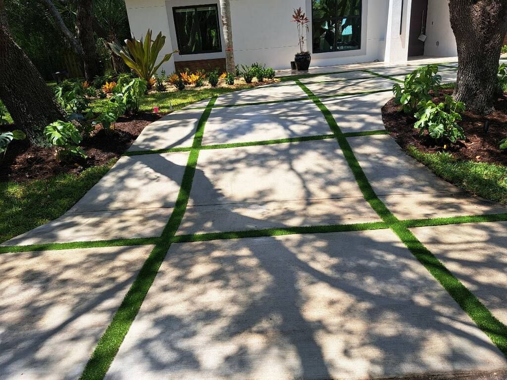 A concrete walkway with green grass between the lines leading to a house.