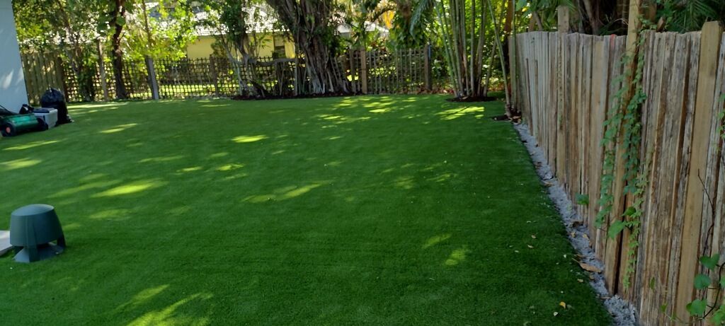 A lawn mower is cutting a lush green lawn next to a wooden fence.