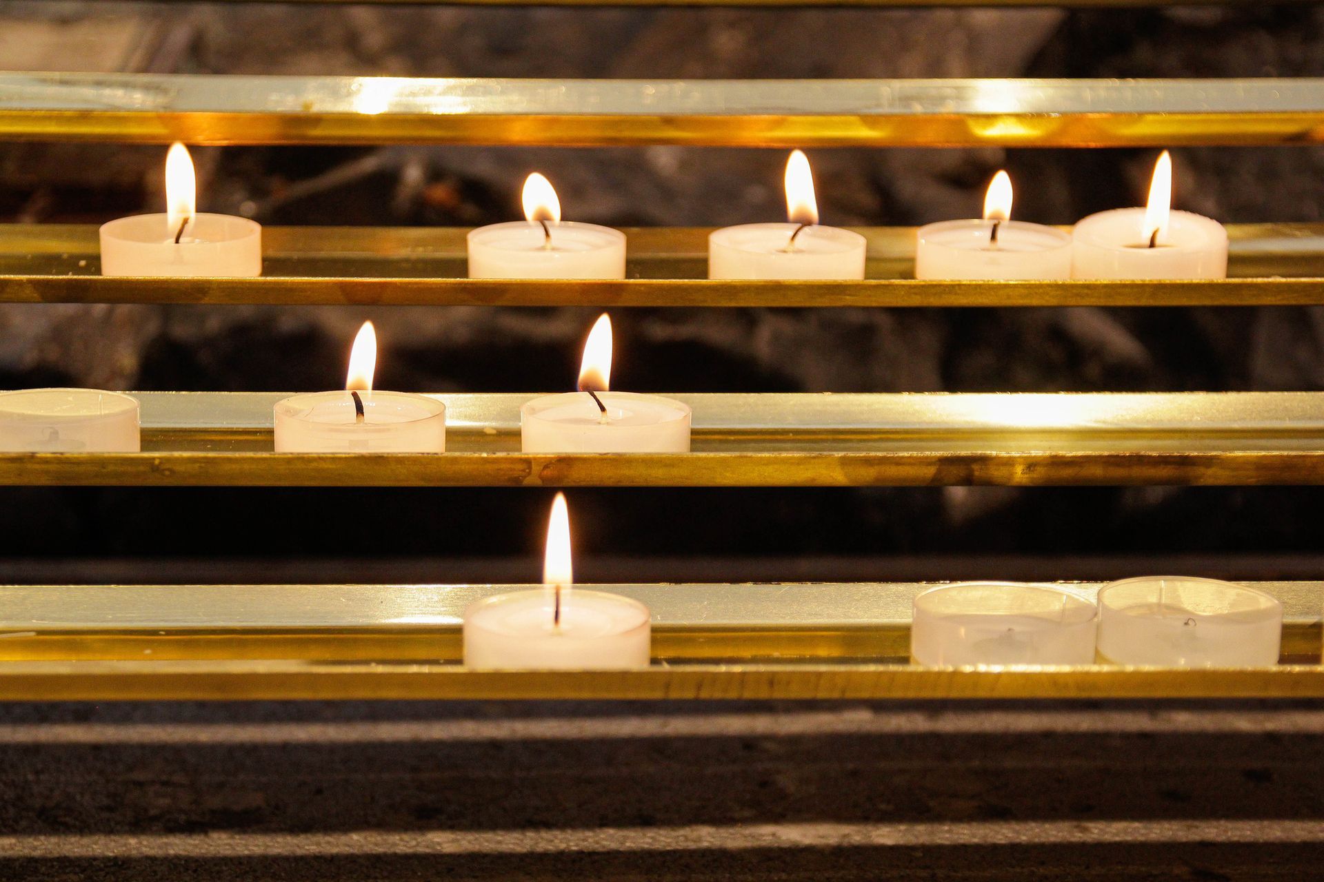 Una fila di candele accese su uno scaffale di ottone