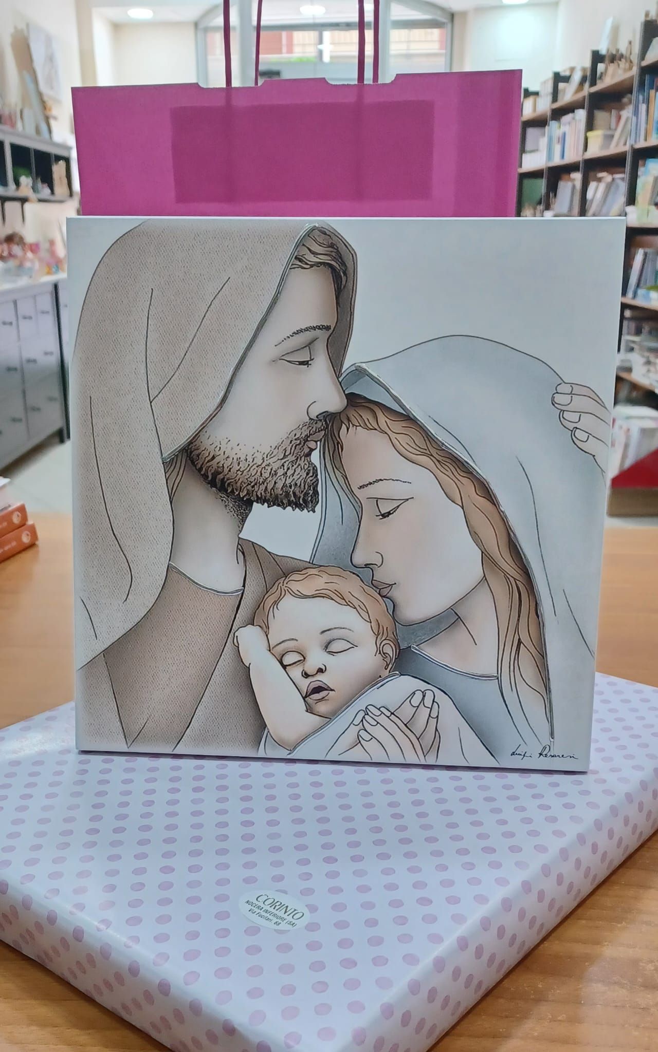Un dipinto di Gesù e Maria che tengono in braccio un bambino è su un tavolo accanto a una borsa rosa.