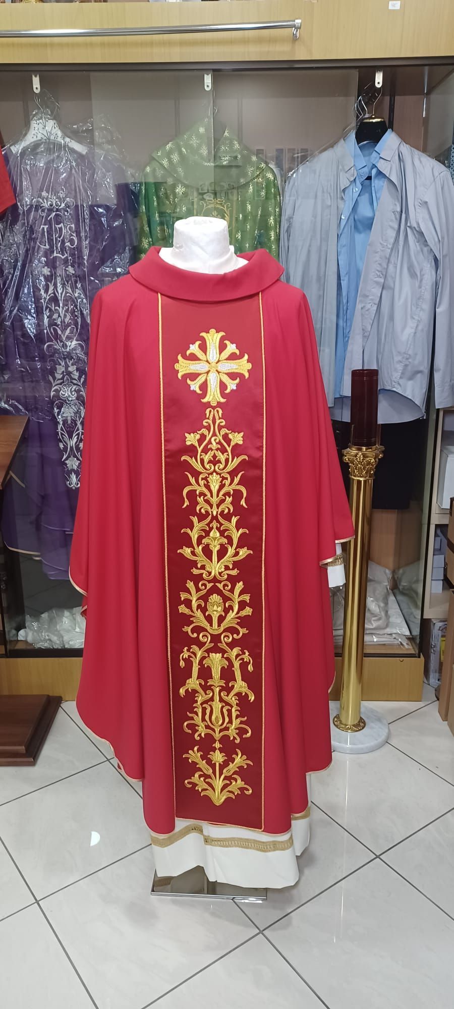 Una pianeta rossa con ricami dorati è su un manichino in un negozio.