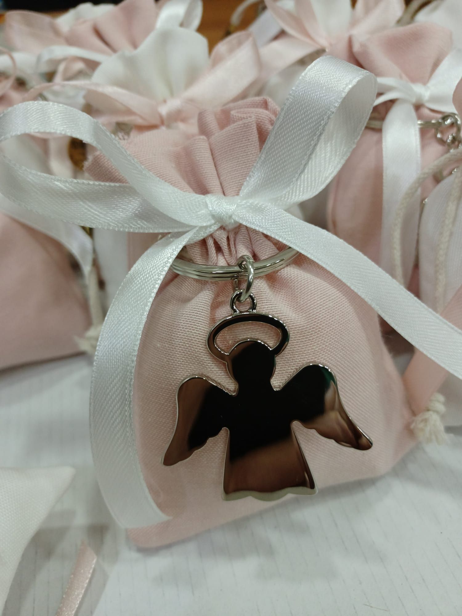 Una borsa rosa con un nastro bianco e un portachiavi con un angelo sopra.