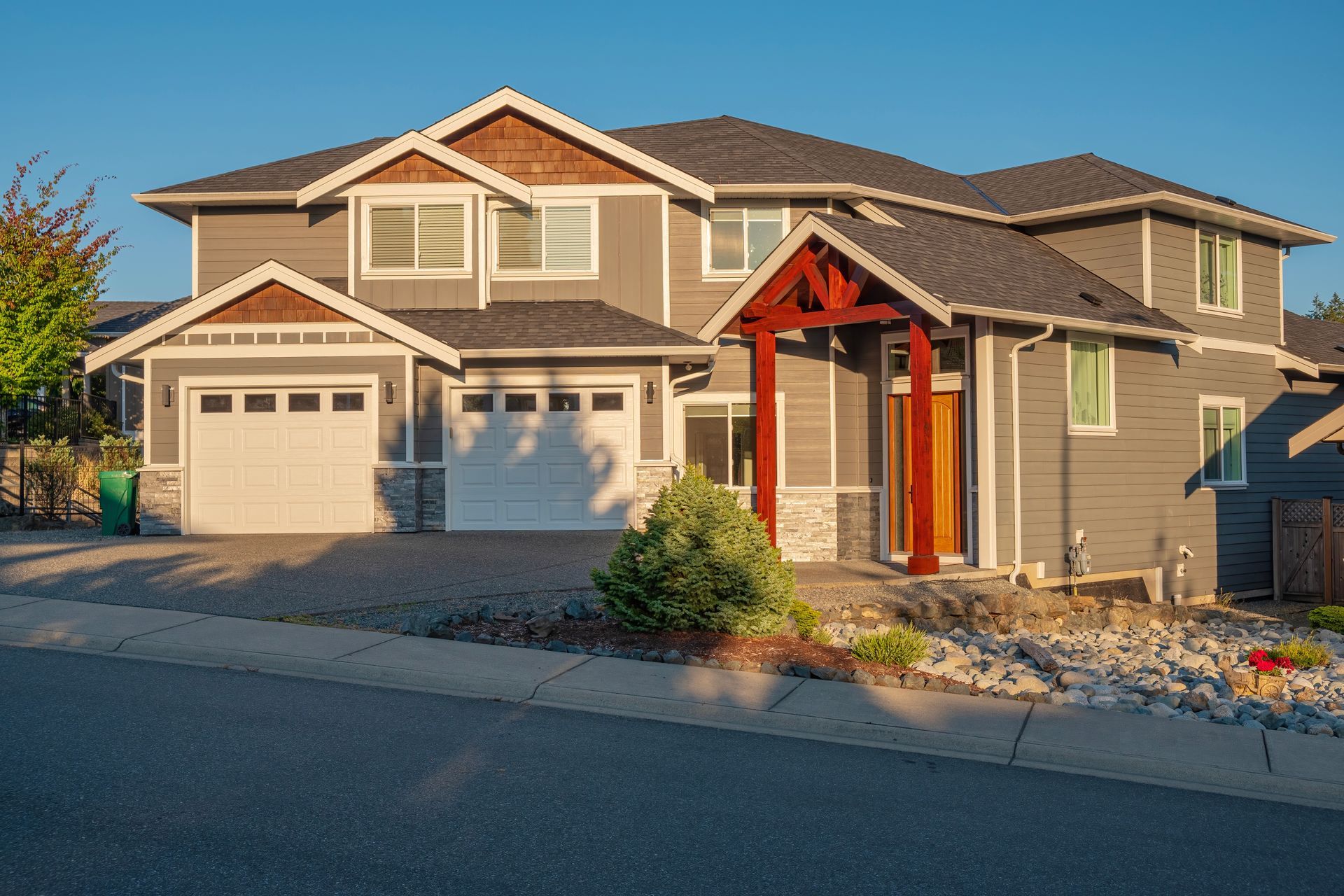 A large gray house with a white garage door is sitting on the side of the road.