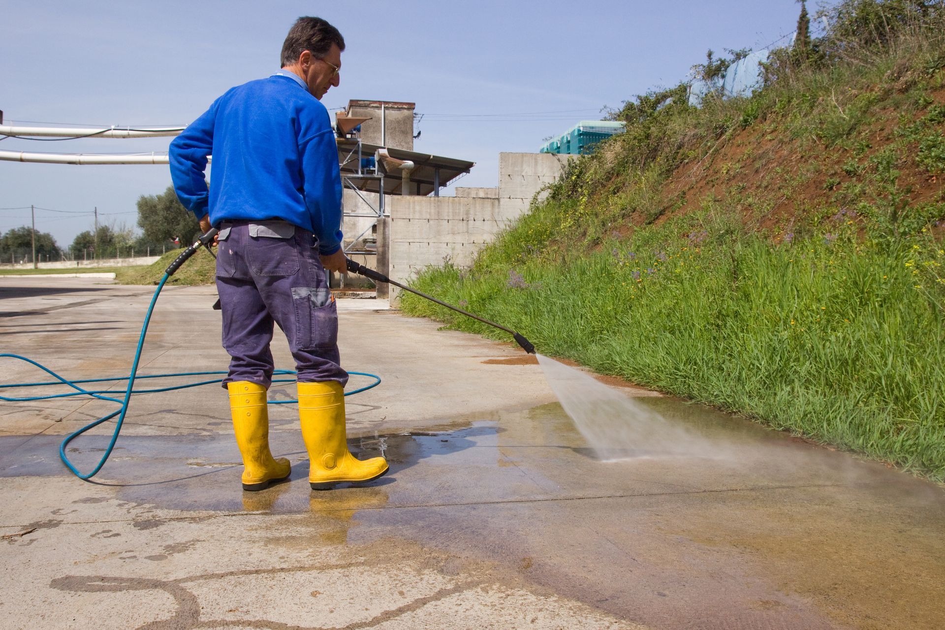 A man wearing yellow boots is using a high pressure washer on a concrete surface.