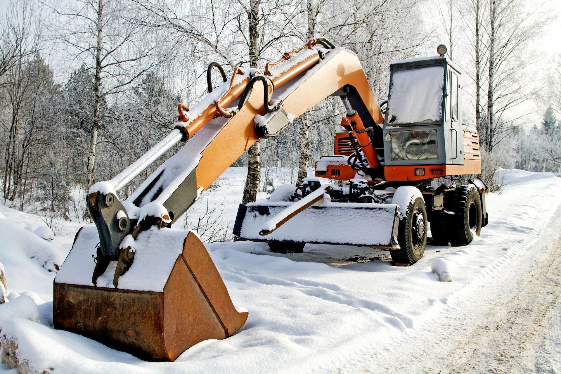 An excavator is parked in the snow on the side of the road