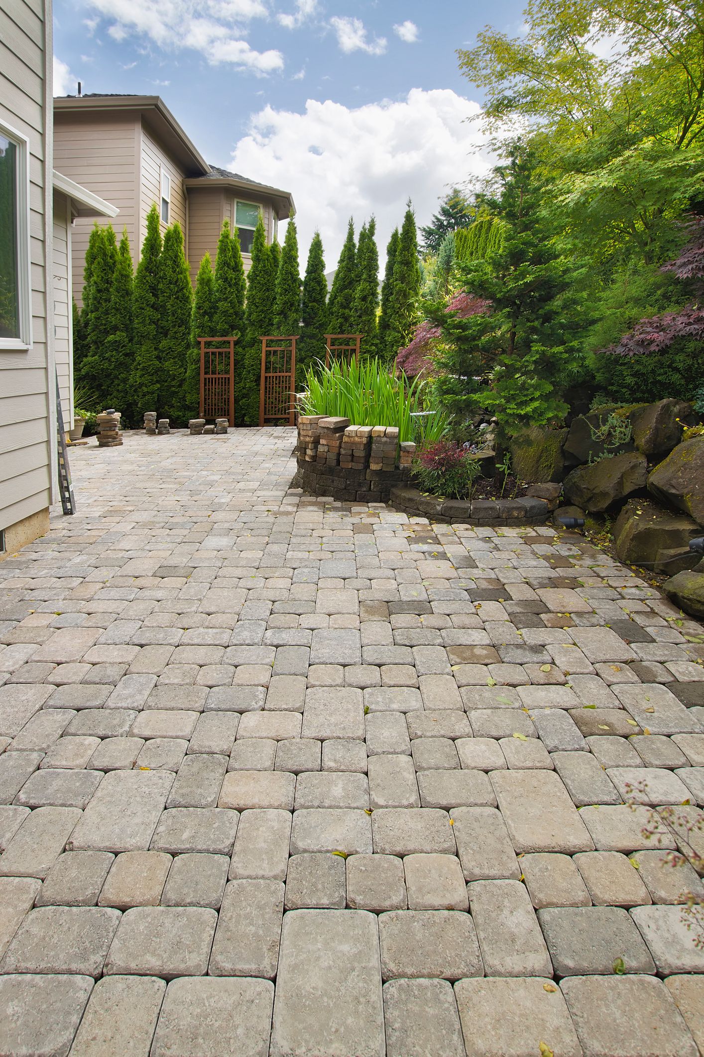 A brick driveway leading to a house with trees in the background.