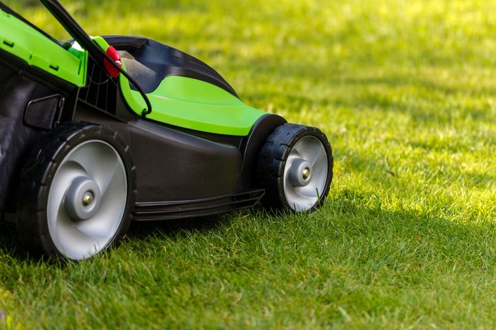 A green and black lawn mower is cutting a lush green lawn.
