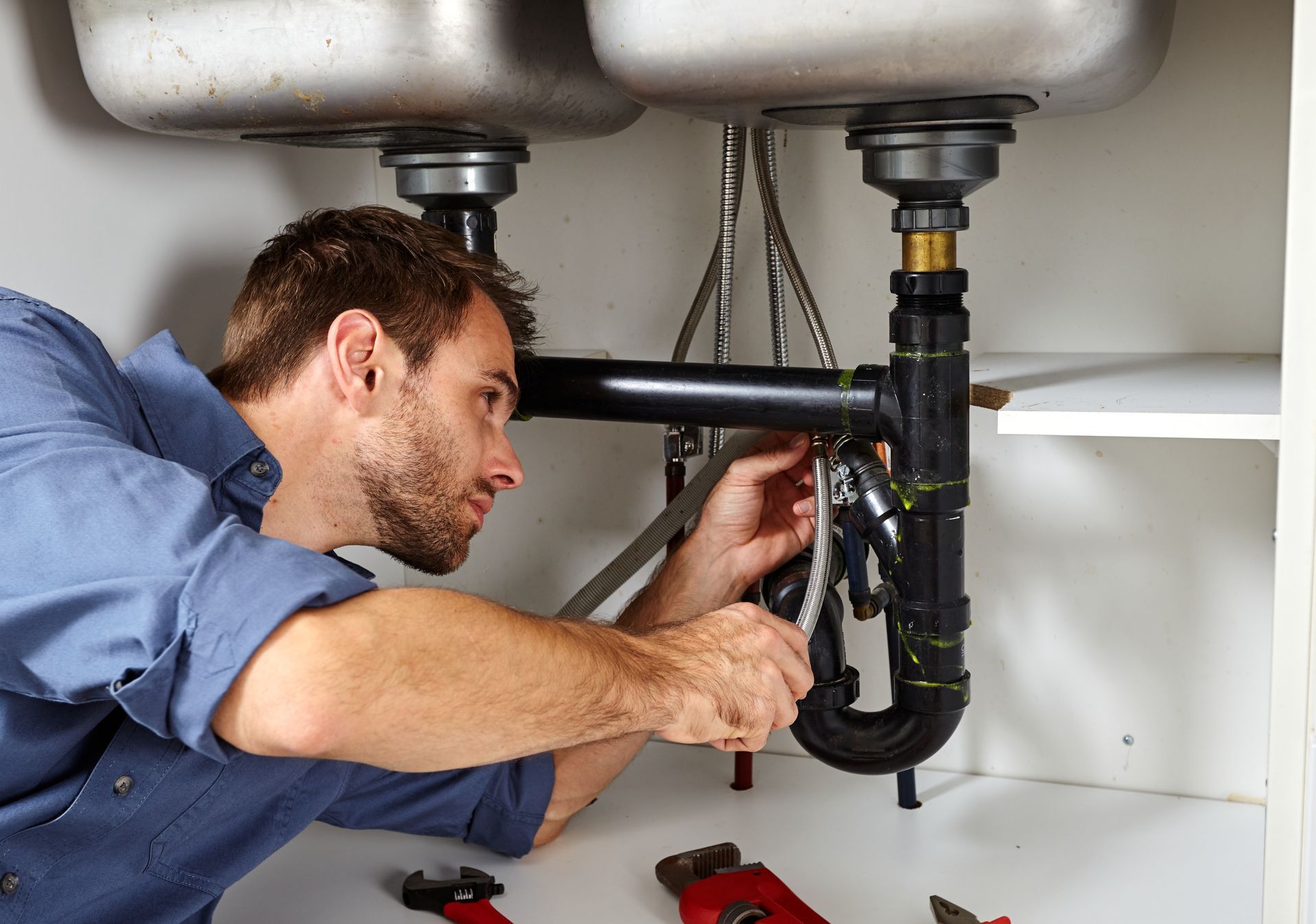 Plumber repairing black sink pipes under a stainless steel basin