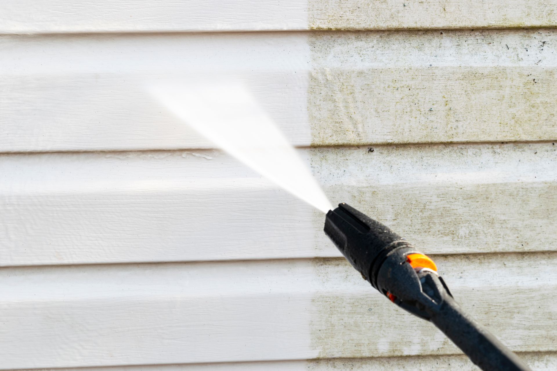 Pressure washing white house siding beside a dirty wall section