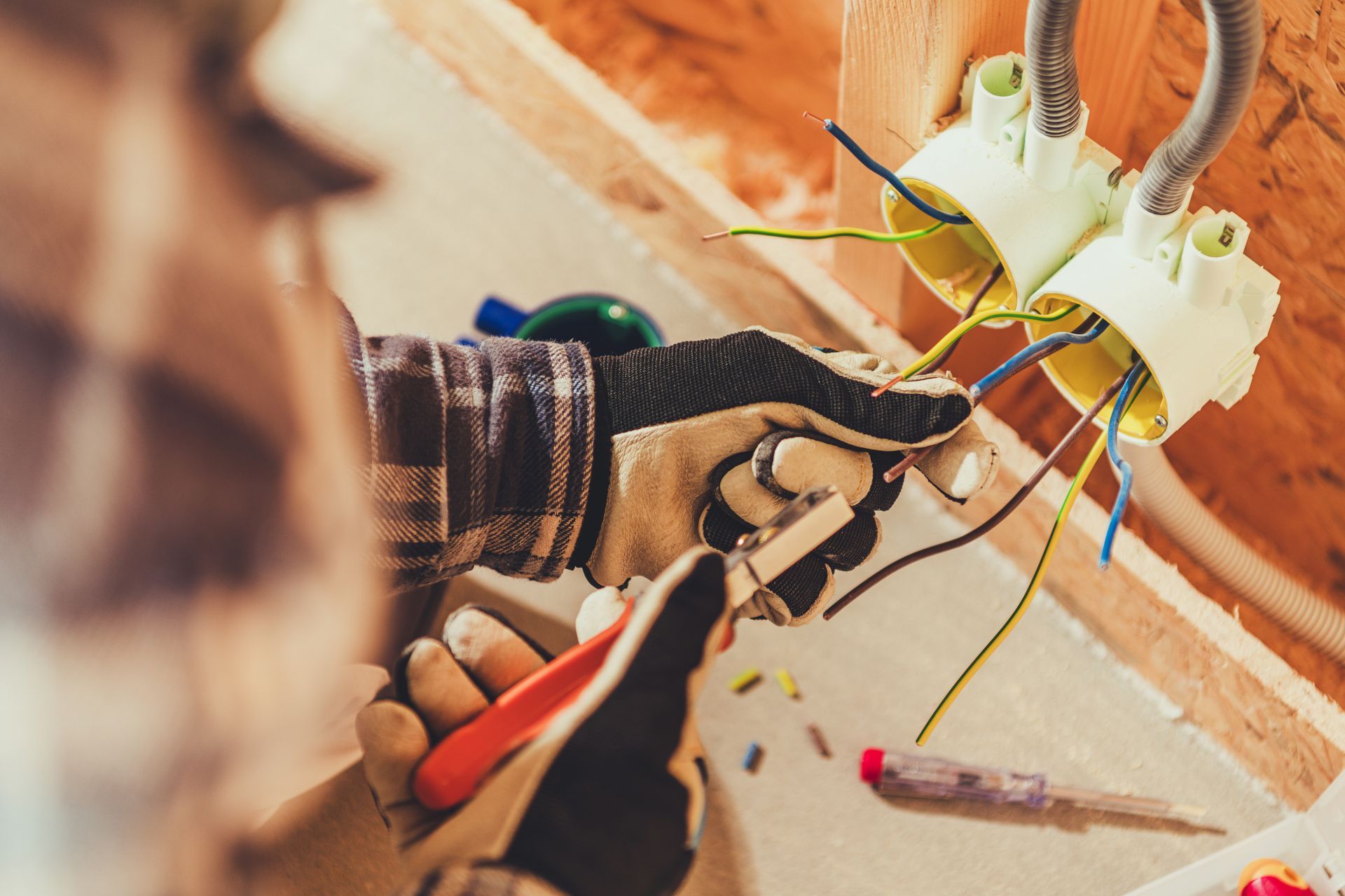 Electrician wiring an electrical outlet with pliers and screwdriver near a wall box.