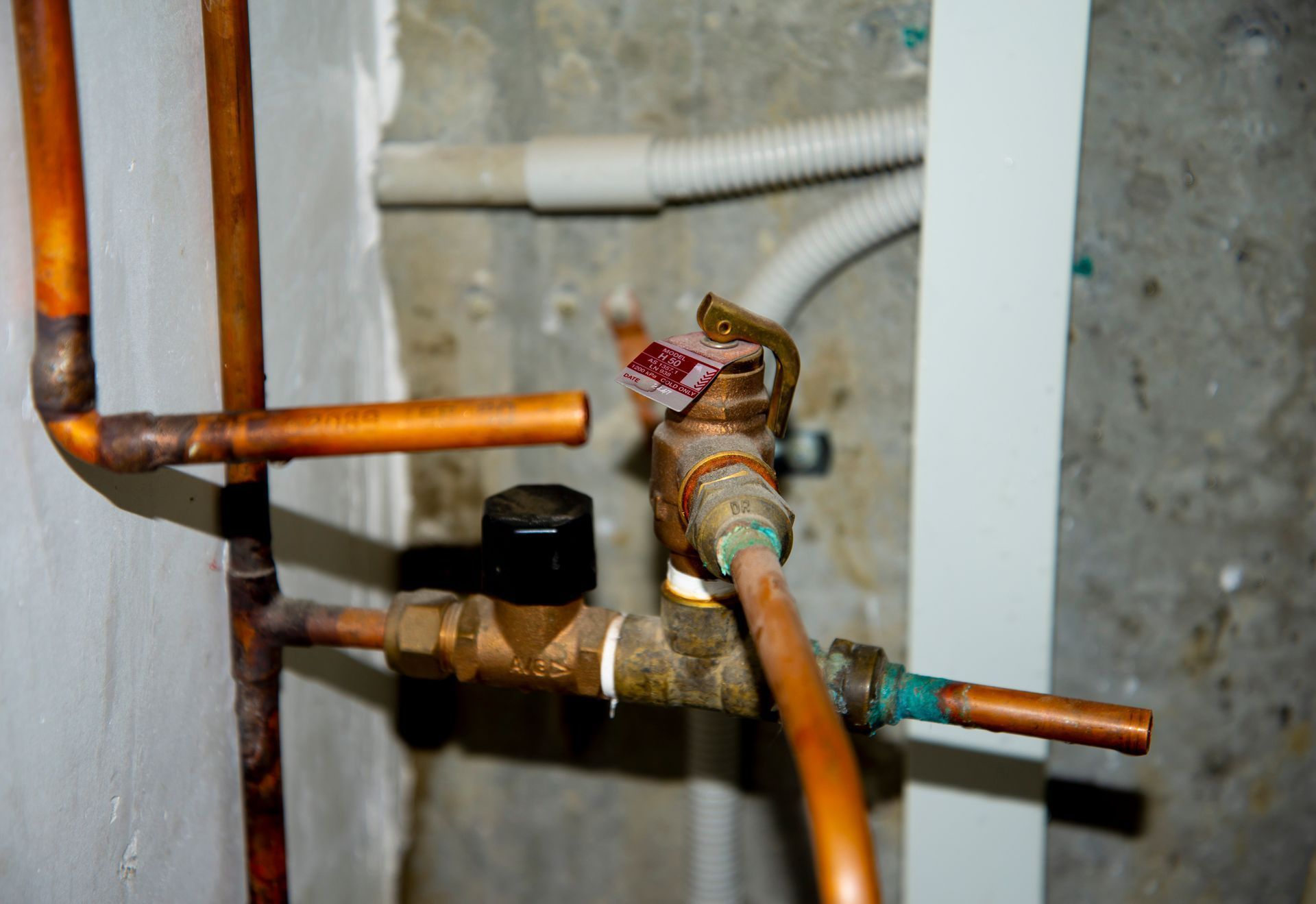 Copper plumbing pipes with valves and fittings against a wall, one pipe capped with tape.