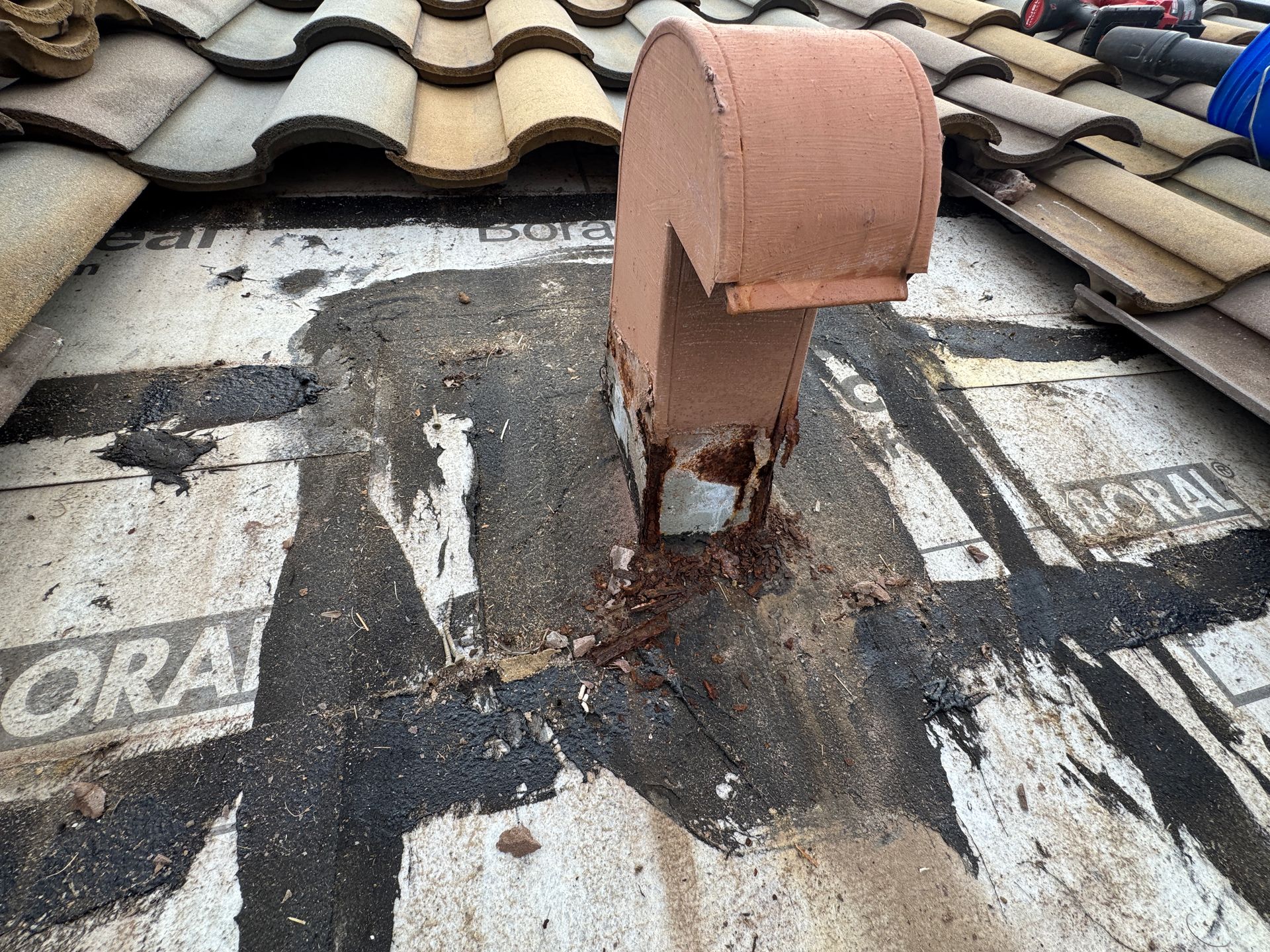 Rusty, peeling orange-painted metal structure at base, near gray pavement; close-up.