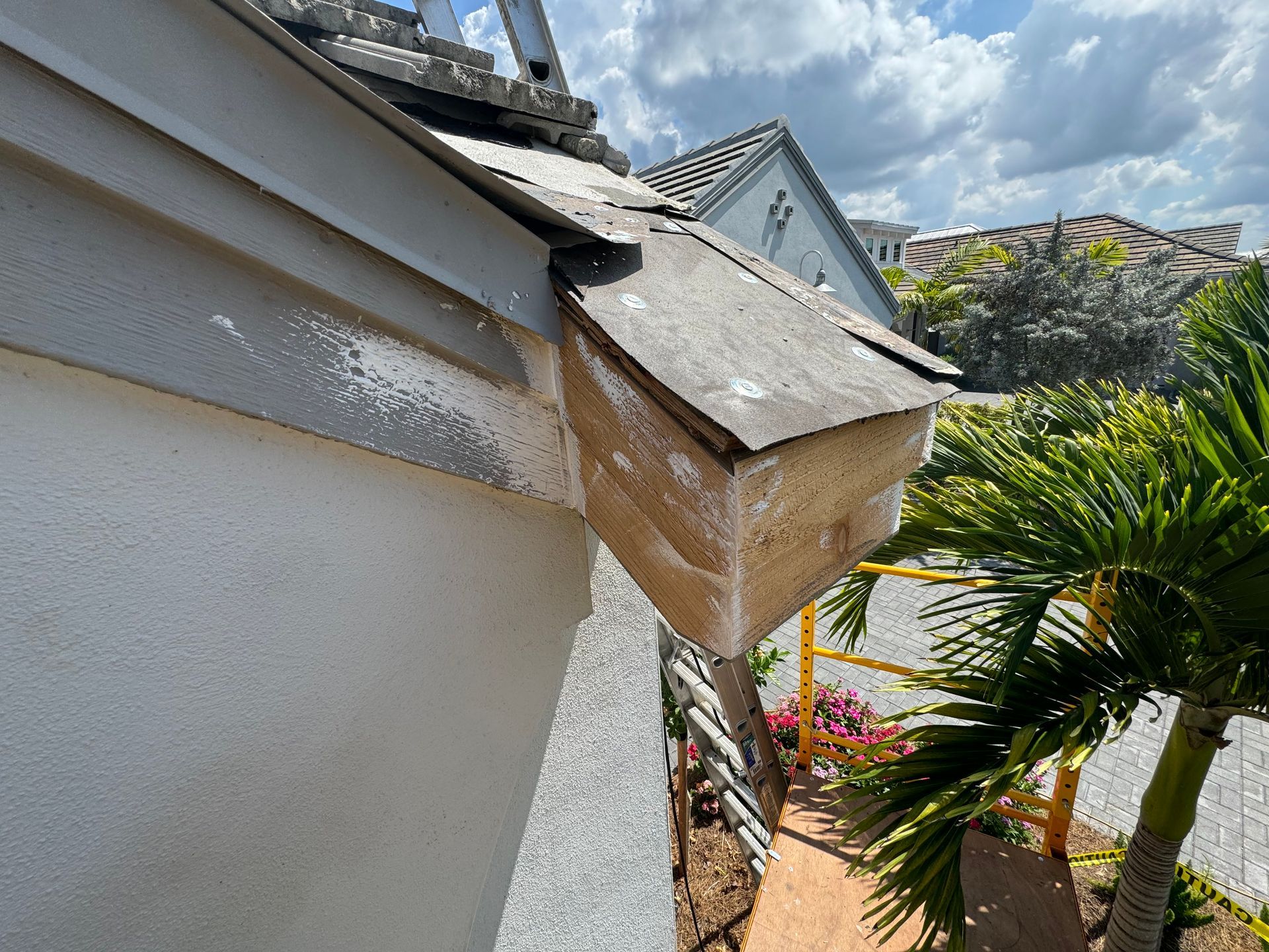 Exterior view of a building with a damaged wooden structure attached to the roof. White building with blue sky.