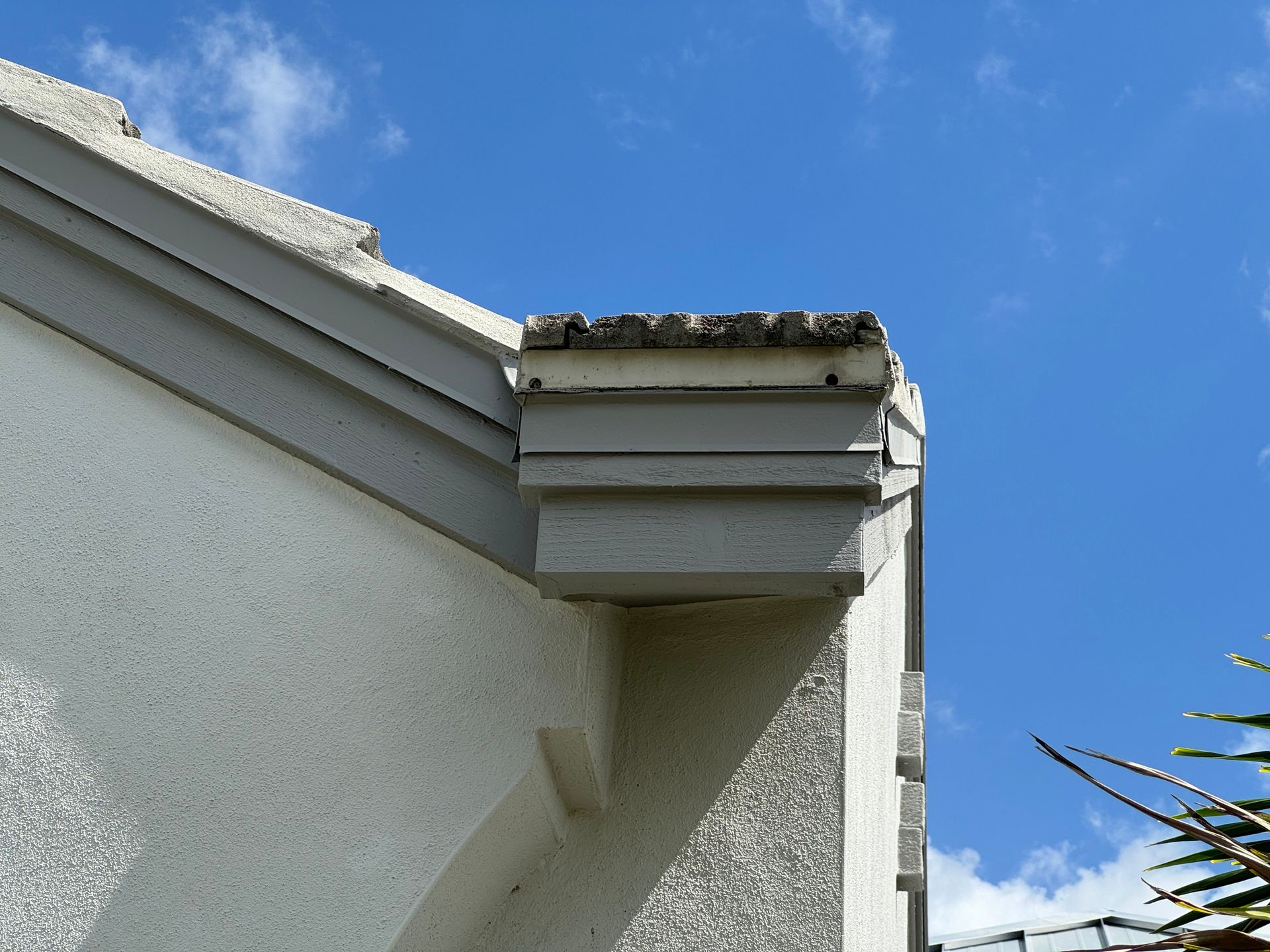 Corner of a building with light gray trim and a textured white wall against a blue sky.