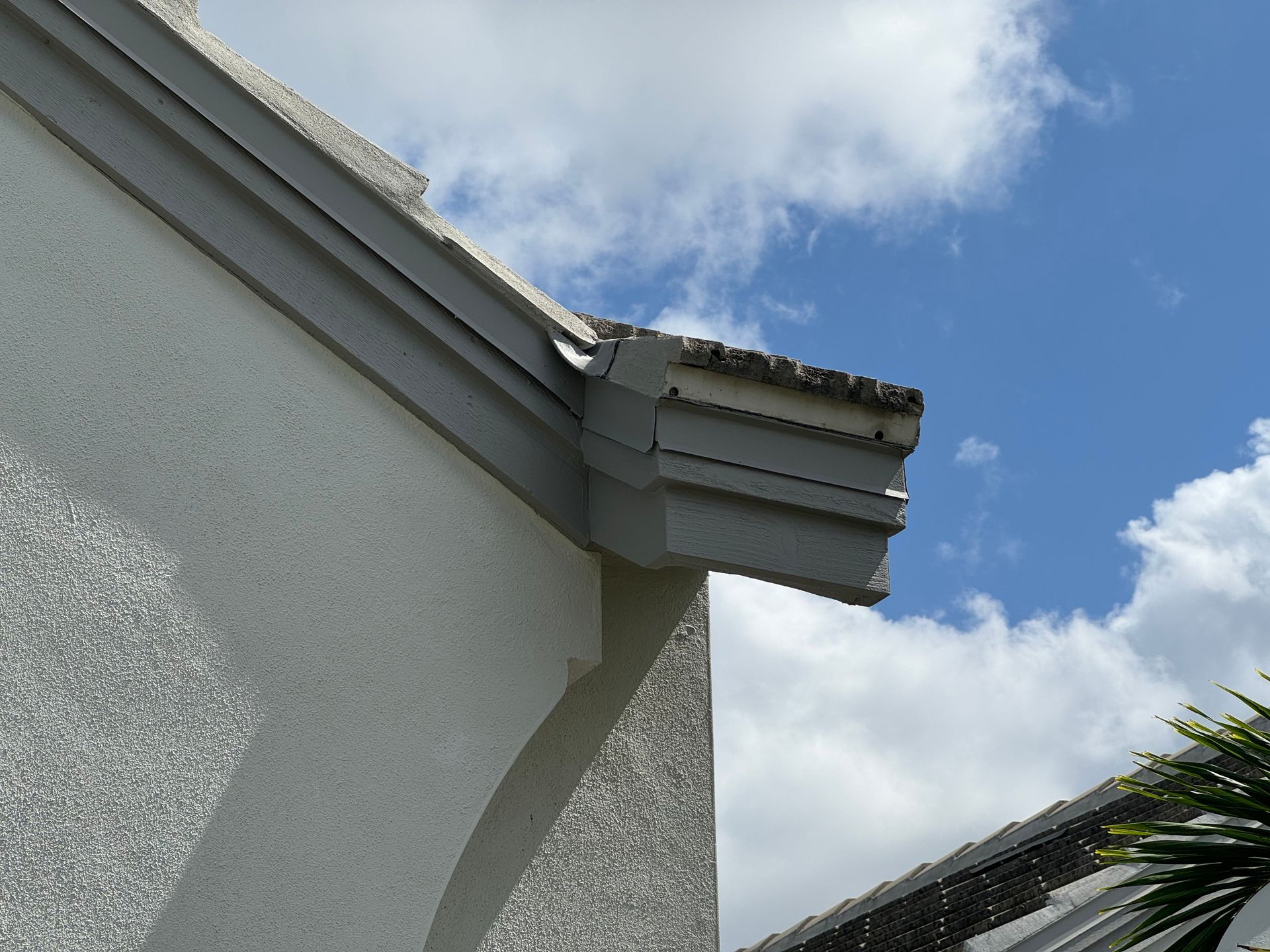 Exterior corner of a building, with gray trim and a cloudy blue sky.