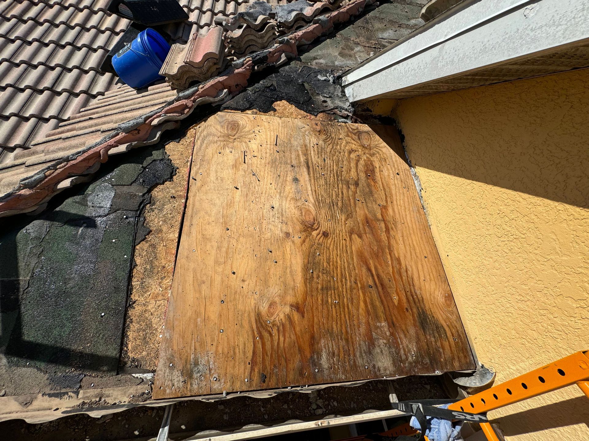 Damaged roof and gutter on a light-colored stucco house; a ladder and scaffolding are set up for repair.