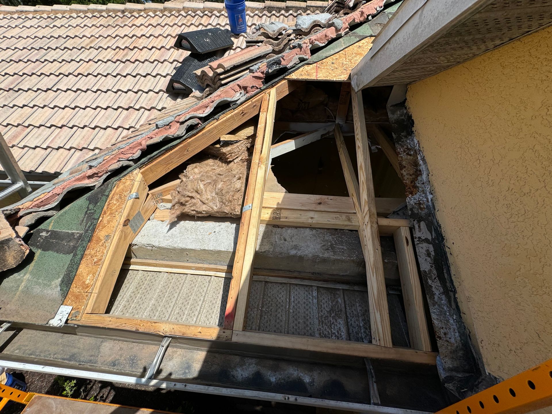 Roof repair: wooden frame exposed on a tiled roof, insulation visible.