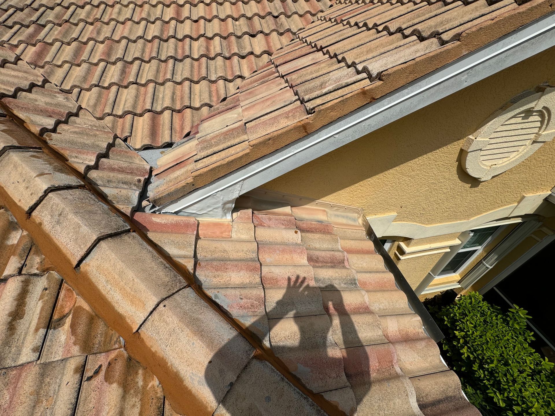 A close-up of a clay tile roof with a shadow of a person taking a photo.