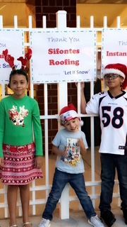 Three children in festive attire stand by a sign that reads 