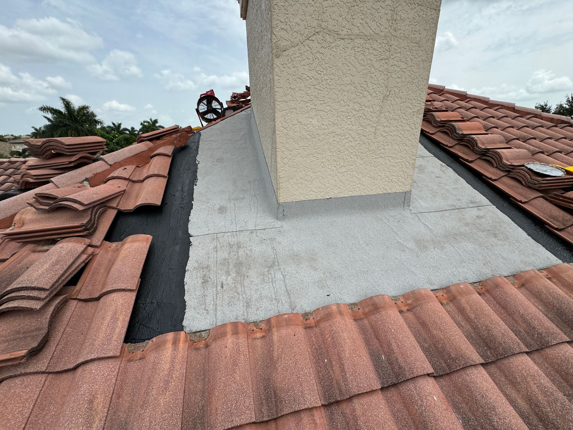 Roof with red tiles and a chimney being worked on by a person.