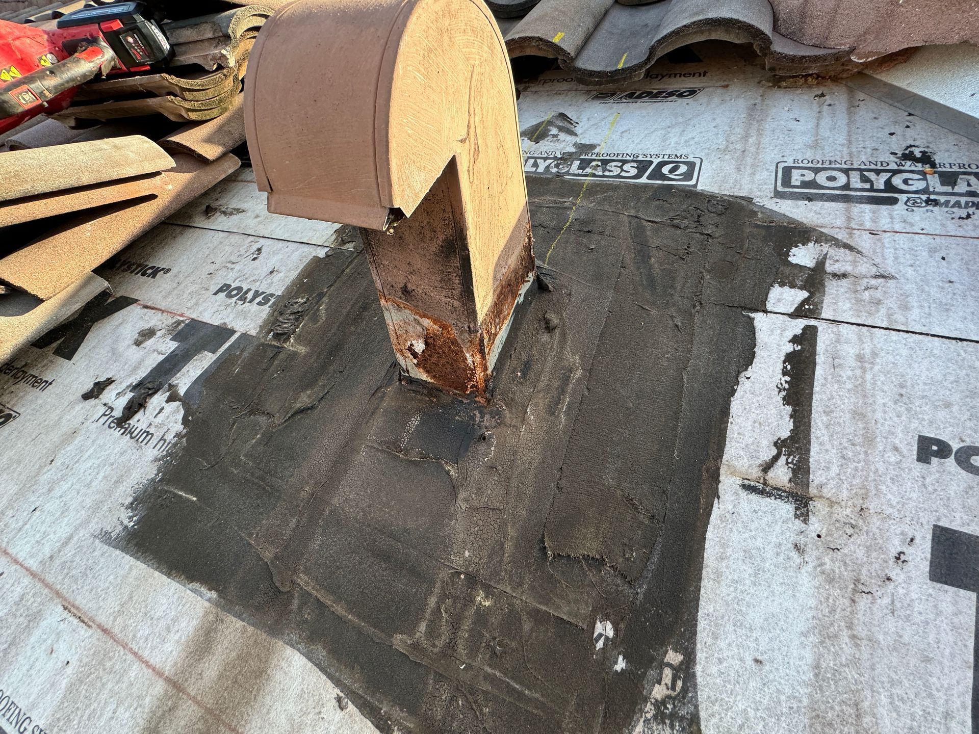 Chimney flashing on a roof, surrounded by roofing material and sealant.